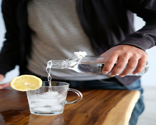 A person pouring water from a jug into a glass next to a laptop